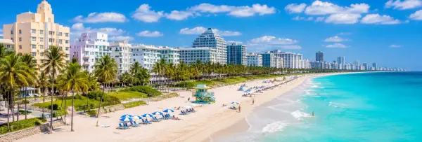 Miami Beach with turquoise ocean, sandy shoreline, palm trees, Art Deco buildings, and beachfront high-rises