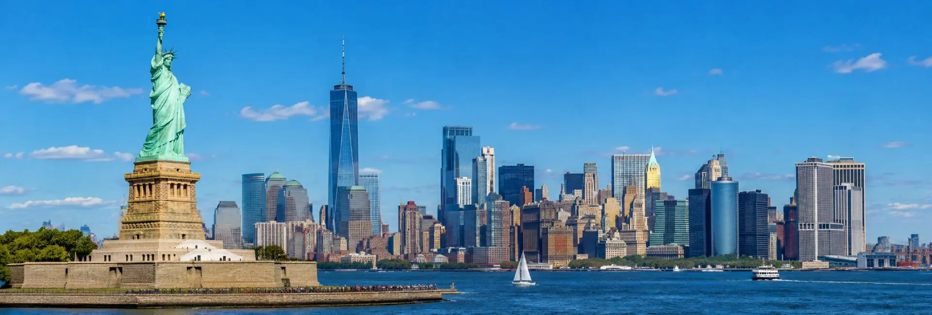 Statue of Liberty with the Lower Manhattan skyline across New York Harbor on a bright sunny day