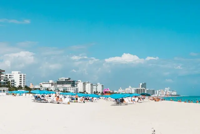 Miami Beach with white sand, blue umbrellas, and oceanfront hotels