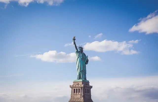 Statue of Liberty standing against a bright blue sky with scattered clouds in New York Harbor
