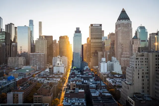 Manhattan skyline viewed from above with skyscrapers and a sunlit avenue stretching through the city