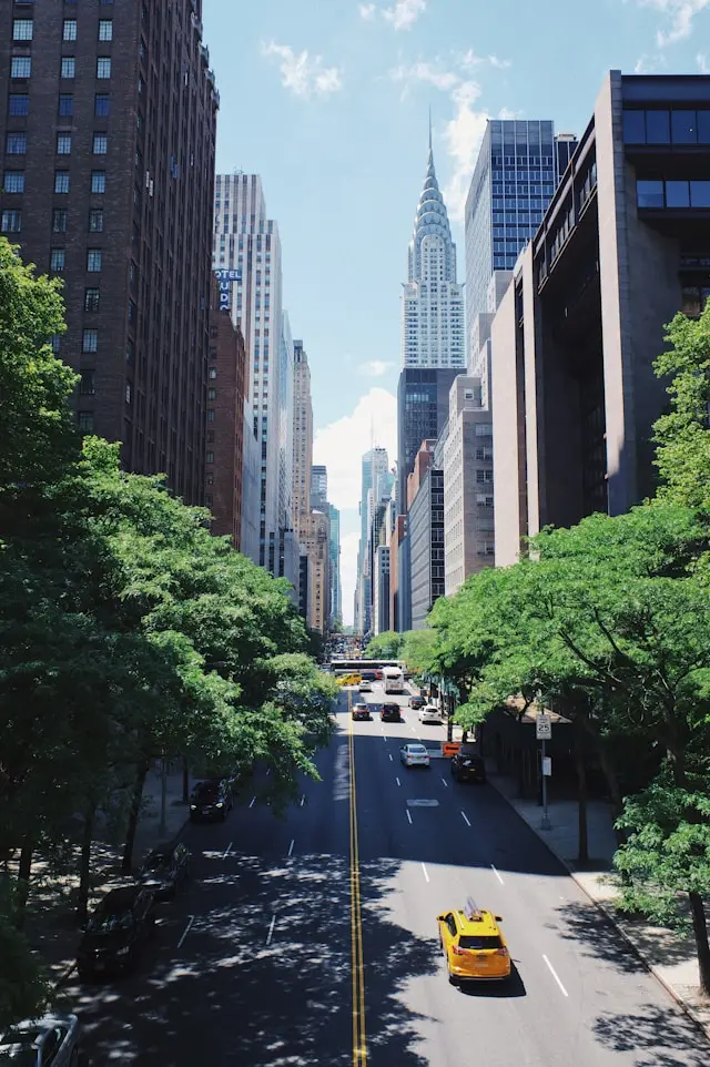 Chrysler Building rising above a tree-lined Manhattan avenue with yellow taxis and city traffic