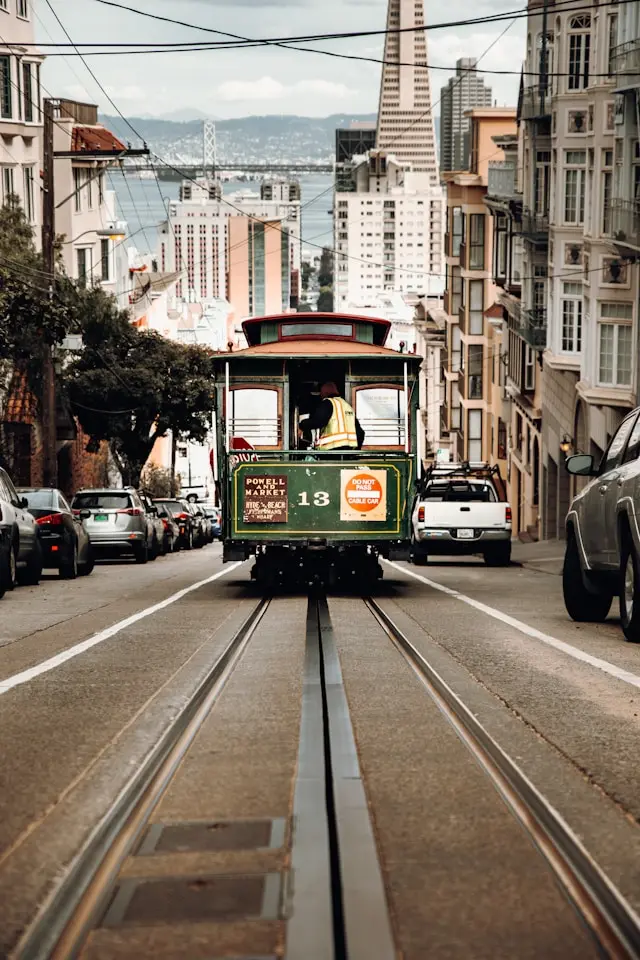 San Francisco cable car traveling down a steep city street with the Bay Bridge in the background